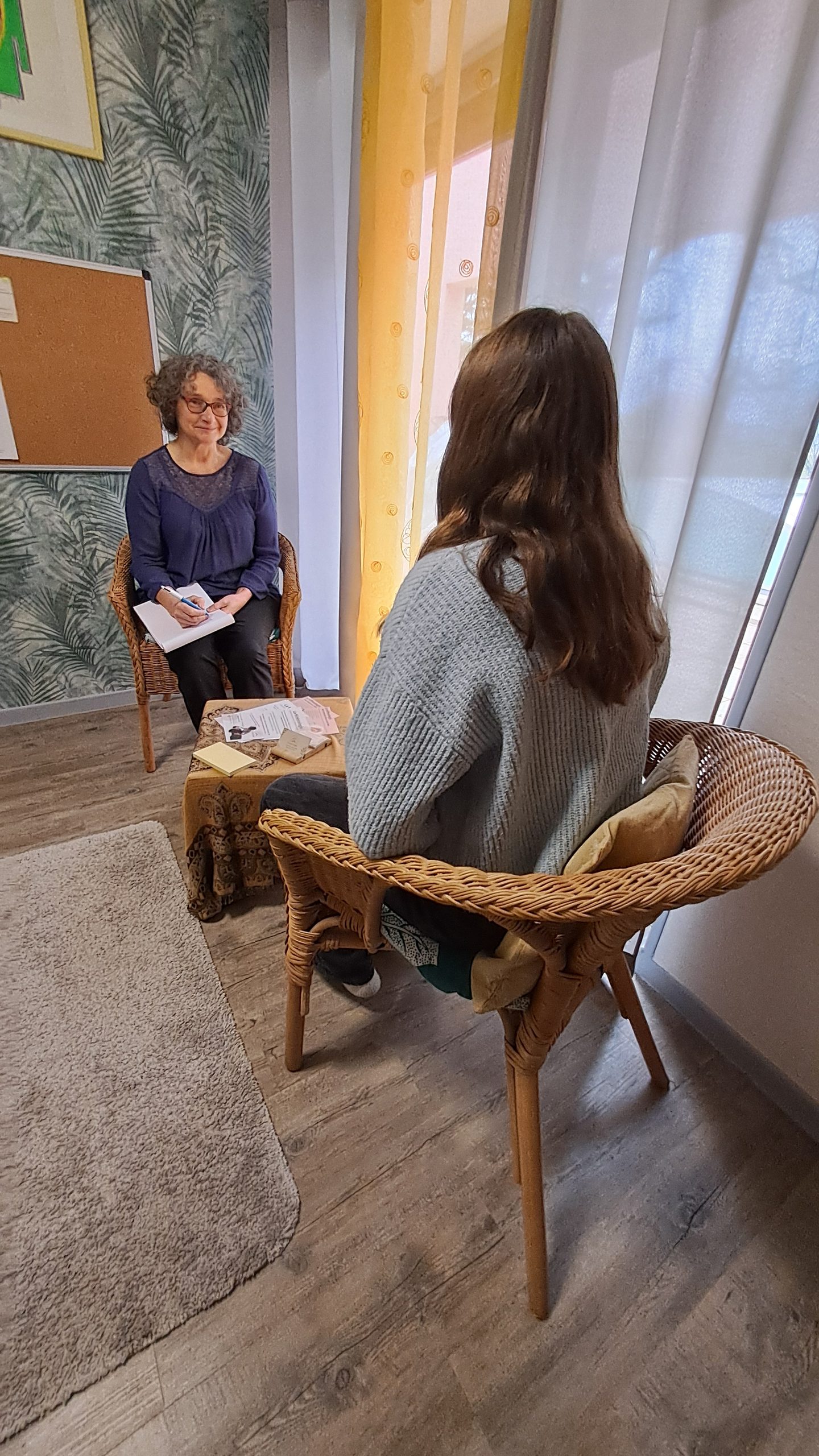 Corinne Card assise face à une personne au cabinet, lors du temps d’échange d’une séance de kinésiologie.